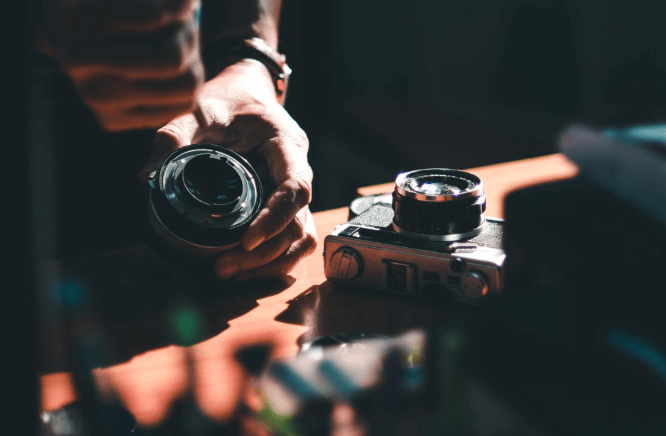 Zbliżenie na fotografa montującego obiektyw na klasycznym, analogowym aparacie fotograficznym