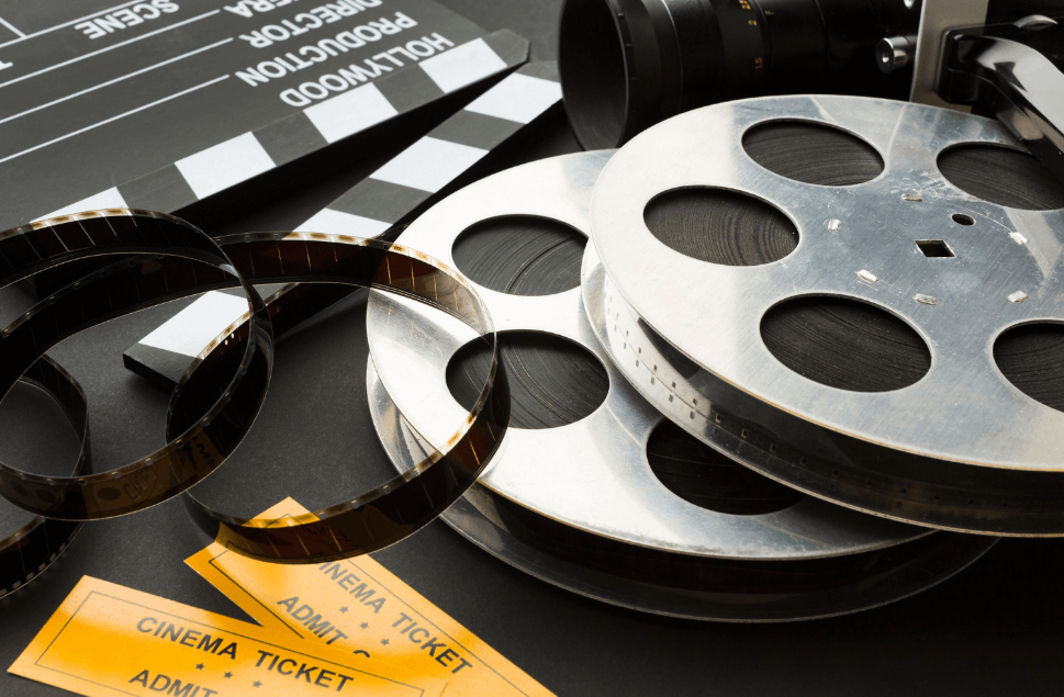 Zbliżenie na sprzęt filmowy: szpule z taśmą filmową, klaps filmowy, i bilety do kina